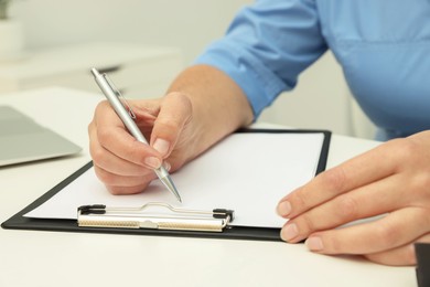 Photo of Doctor writing diagnosis at white table, closeup