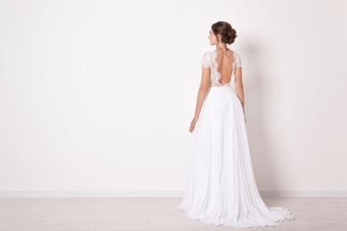 Young bride wearing beautiful wedding dress near light wall. Space for text