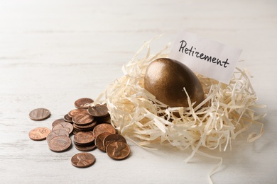 Golden egg and card with word RETIREMENT in nest near coins on wooden background. Pension concept