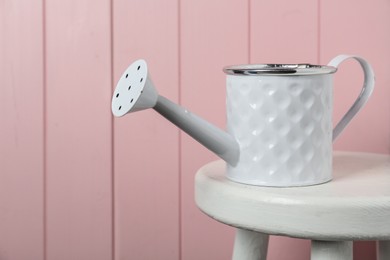 Photo of White metal watering can on table against pink wooden background