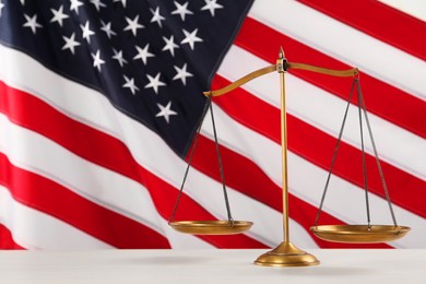 Scales of justice on white wooden table against American flag, space for text