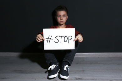 Abused little boy with hashtag STOP near black wall. Domestic violence concept