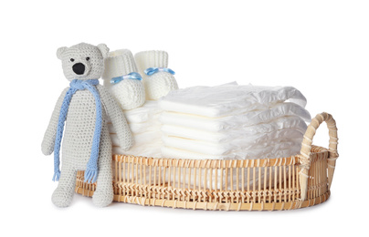 Photo of Wicker tray with disposable diapers, toy bear and child's booties on white background