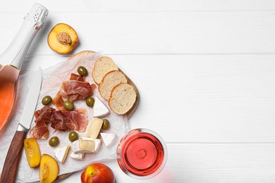 Photo of Delicious rose wine and snacks on white wooden table, flat lay. Space for text