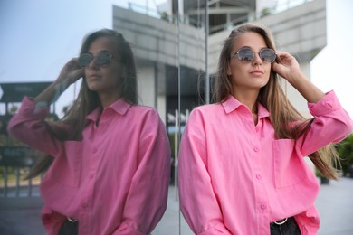 Beautiful young woman in stylish sunglasses near building outdoors