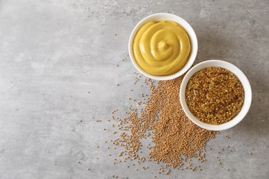 Photo of Bowls with mustard and seeds on grey table, flat lay. Space for text