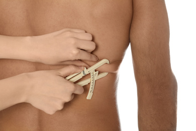 Nutritionist measuring man's body fat layer with caliper on white background, closeup