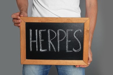 Photo of Man holding small chalkboard with word Herpes on grey background
