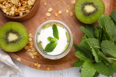 Photo of Delicious dessert with kiwi, yogurt and mint on wooden board, flat lay