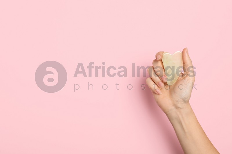 Photo of Woman with jade gua sha tool on light pink background, closeup. Space for text