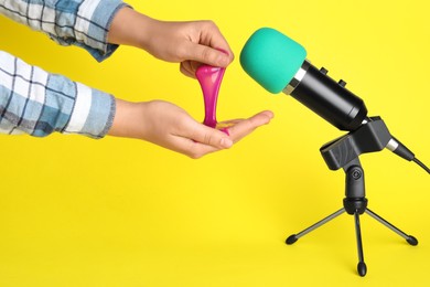 Woman making ASMR sounds with microphone and bright slime on yellow background, closeup