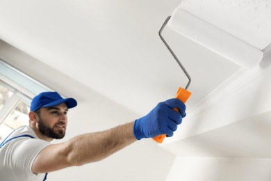 Handyman painting ceiling with white dye indoors, focus on roller