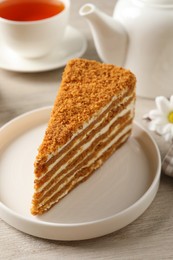 Slice of delicious layered honey cake served with tea on wooden table, closeup