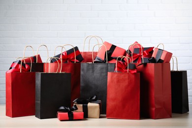 Paper shopping bags and gift boxes on table near white brick wall. Black Friday sale