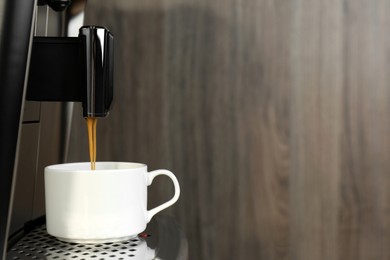 Modern espresso machine pouring coffee into cup on wooden background, closeup. Space for text