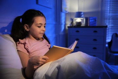 Little girl reading fairy tale in dark bedroom
