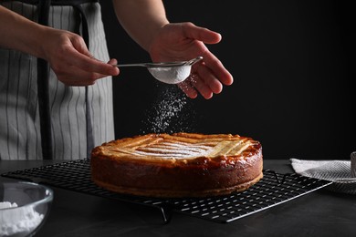 Woman decorating tasty apricot pie with powdered sugar at black table, closeup