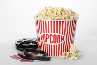 Bucket of fresh popcorn, tickets and movie reel on white background. Cinema snack