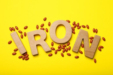 Word Iron and pills on yellow background, flat lay. Anemia treatment