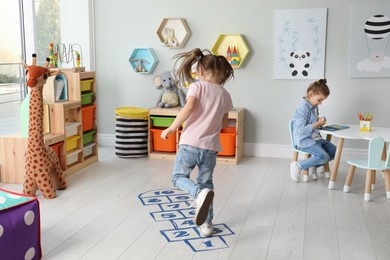 Photo of Cute little girls playing hopscotch at home