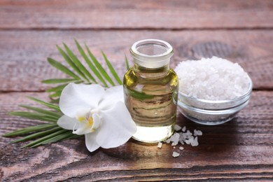 Bottle of essential oil, sea salt and orchid flower on wooden table, closeup