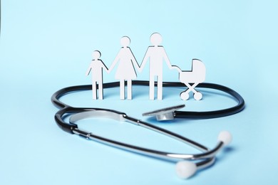 Photo of Figures of family stainding near stethoscope on light blue background. Insurance concept