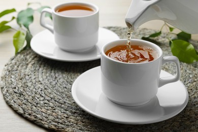 Pouring green tea into white cup with saucer on table, closeup