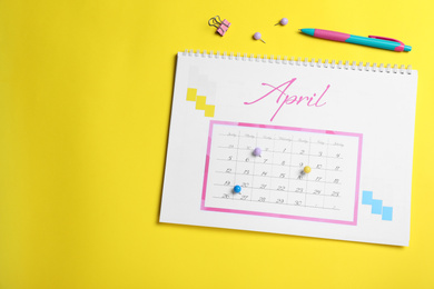 Calendar page marked with drawing pins on yellow background, flat lay