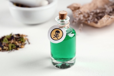 Glass bottle of poison with warning sign on light background