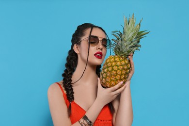 Photo of Young woman with fresh pineapple on light blue background. Exotic fruit
