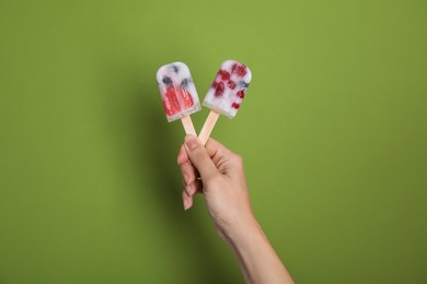 Woman holding berry popsicles on green background, closeup