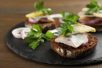 Photo of Delicious sandwiches with salted herring, onion rings, parsley and lemon on wooden table, closeup