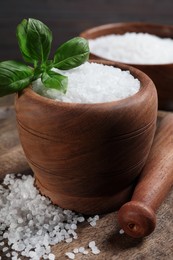 Pestle and mortar with natural sea salt on wooden table, closeup