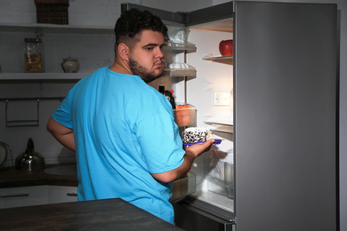 Depressed overweight man taking cake out of refrigerator at night