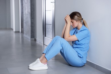 Exhausted doctor sitting on floor in hospital, space for text