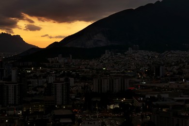 Photo of Picturesque view of sunset with dark clouds above big mountains and city