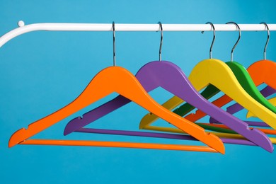 Bright clothes hangers on metal rail against light blue background, closeup