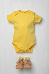 Child's bodysuit and booties on white wooden background, flat lay