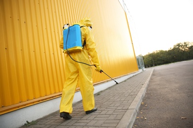 Person in hazmat suit disinfecting street with sprayer, back view. Surface treatment during coronavirus pandemic