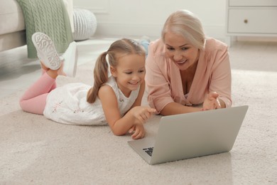 Photo of Happy grandmother and her granddaughter using  laptop together on floor at home