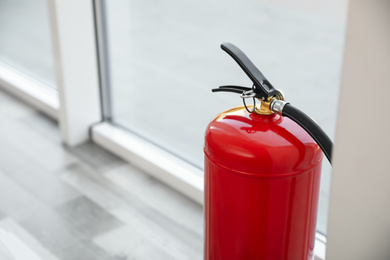Fire extinguisher near window indoors, closeup. Space for text