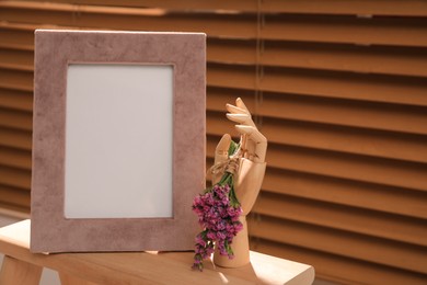 Empty photo frame and decorative hand with flowers on wooden table indoors, space for text