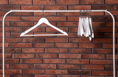 Photo of White clothes hangers on rack near red brick wall. Space for text
