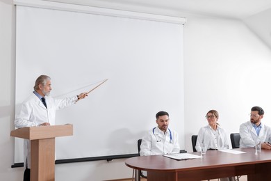 Photo of Senior doctor giving lecture in conference room with projection screen