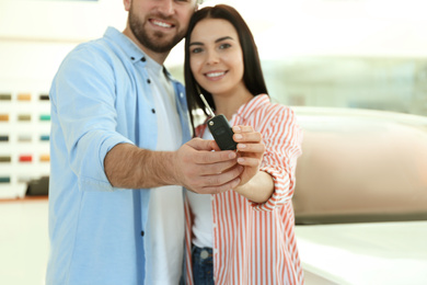 Happy couple with car key in modern auto dealership, focus on hands