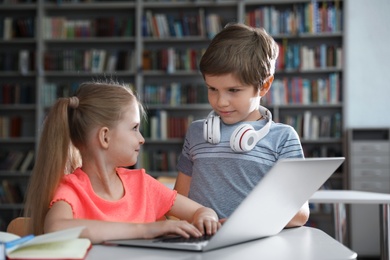 Little boy with headphones and girl reading book using laptop in library