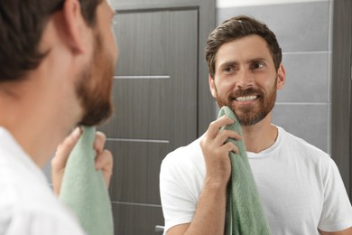 Handsome man drying his beard in front of mirror in bathroom