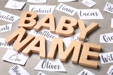 Paper sheets with different baby names, and wooden letters on grey background, closeup