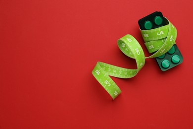 Weight loss pills and measuring tape on red background, top view. Space for text