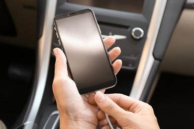 Photo of Woman connecting charging cable to smartphone in car, closeup
